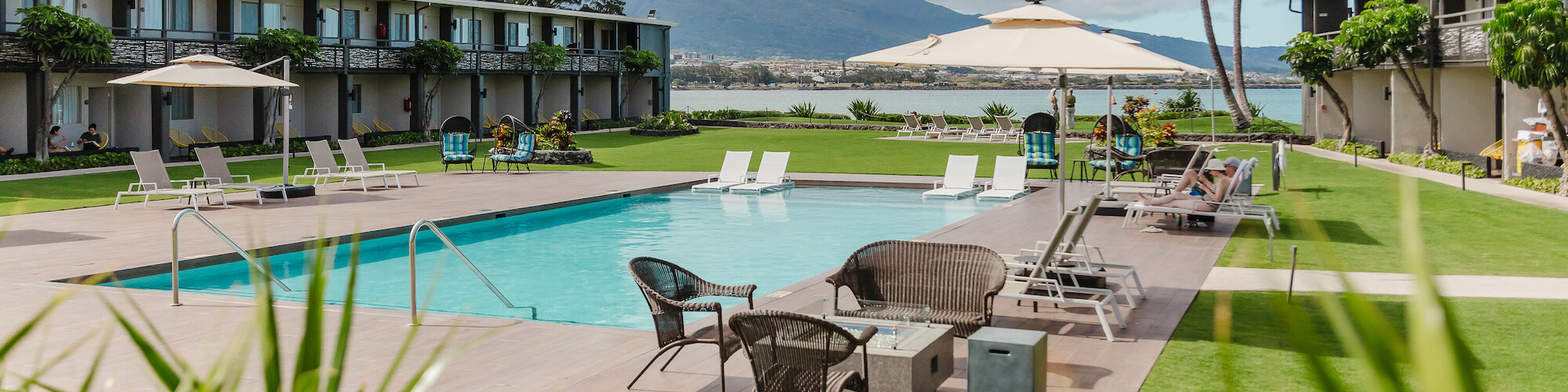 The image shows a hotel courtyard with a pool, surrounded by lounge chairs and palm trees, with mountains in the background.