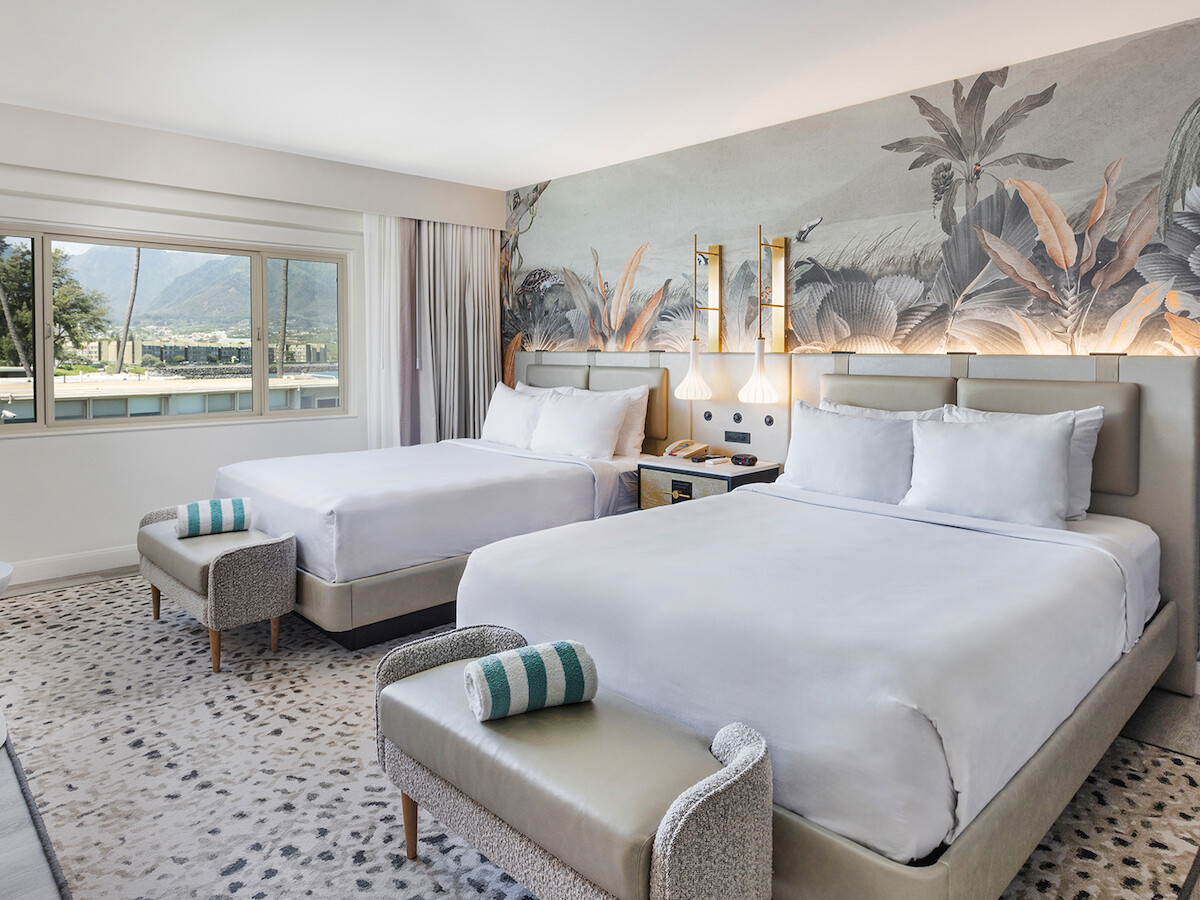 The image shows a hotel room with two double beds, a nature-themed mural, modern decor, and a window with a scenic view.