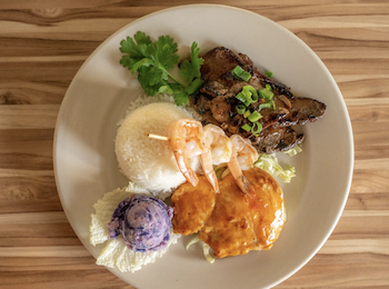 A plate with grilled shrimp, beef, rice, potato scoop, and garnish on a wooden table.