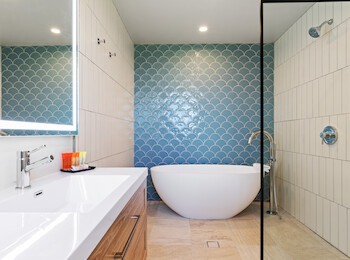 Modern bathroom with a freestanding tub, blue fish scale tiles, white sink with orange accessories, and wood cabinet.