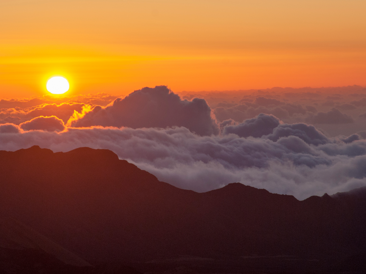 A vibrant sunrise over a mountainous landscape with clouds, casting warm hues across the sky.