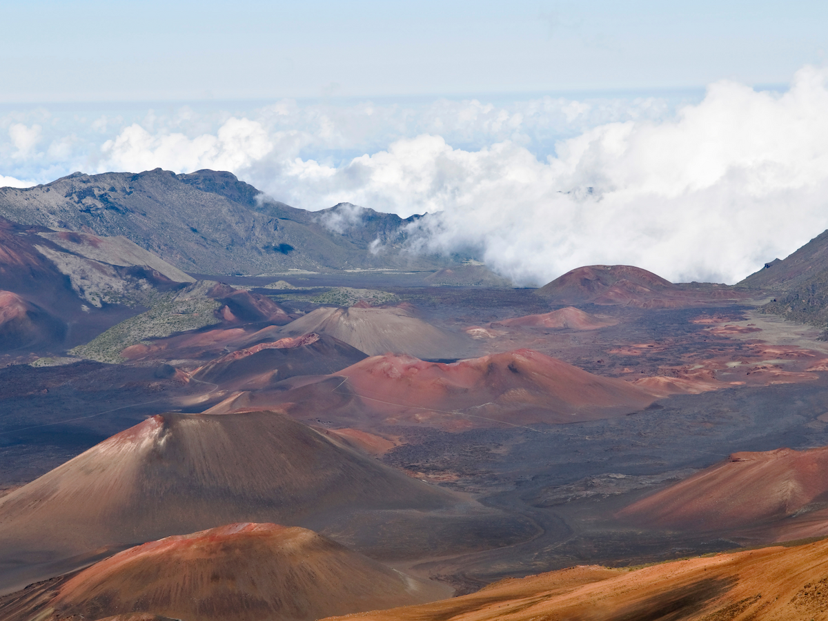 The image shows a volcanic landscape with multiple craters and reddish-brown terrain, under a partly cloudy sky.