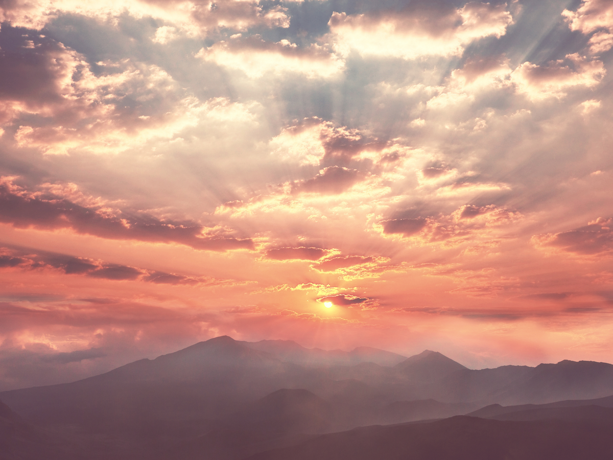 A breathtaking sunset over mountains with dramatic clouds and sun rays creating a serene and beautiful landscape.
