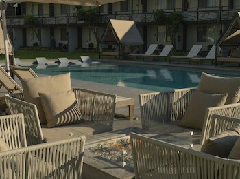 Poolside seating with chairs, cushions, and a central table near a pool, surrounded by lounge chairs and cabanas in the background.