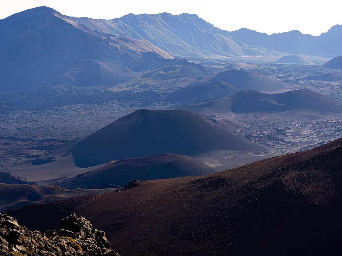 The image shows a mountainous landscape with rolling hills and rocky terrain under a clear sky.