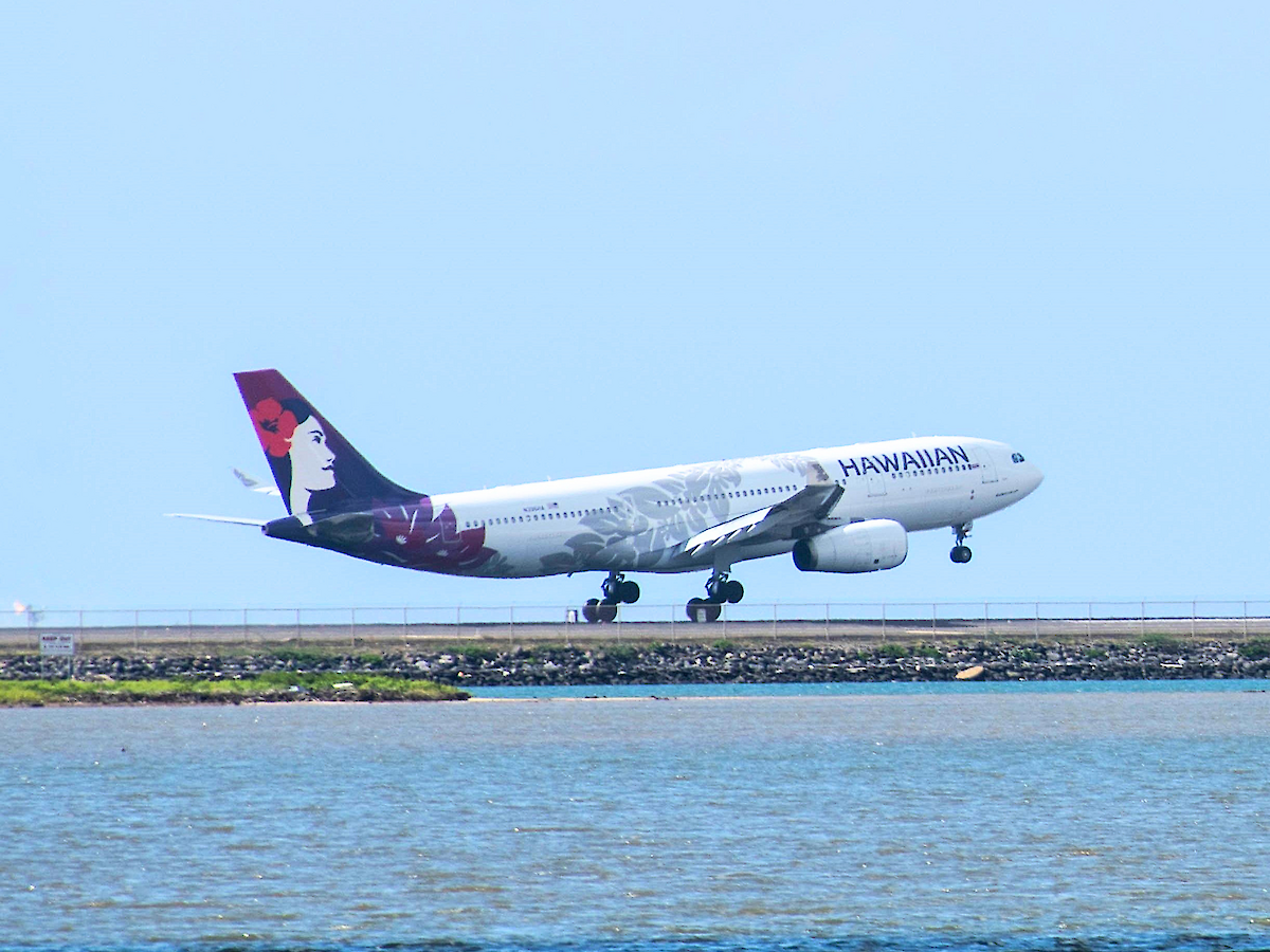 An airplane is taking off from a runway beside a body of water, against a clear blue sky.
