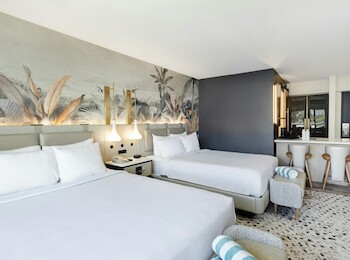 A hotel room with two beds, a nature-themed mural, a small seating area, and a kitchenette.