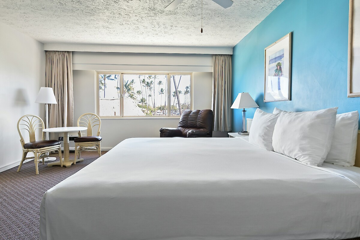 A hotel room with a bed, a small dining area, a window, and artwork on a blue accent wall.