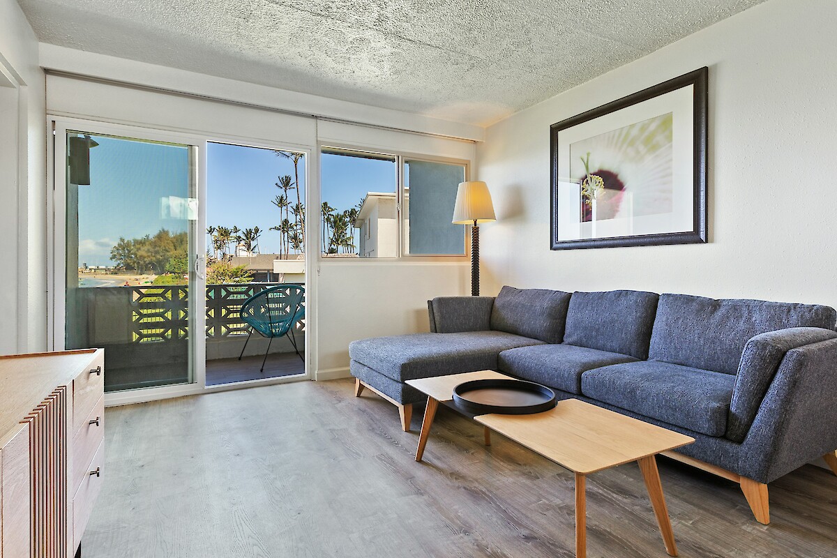 A modern living room with a gray sectional sofa, coffee table, lamp, artwork, and glass doors leading to a balcony.