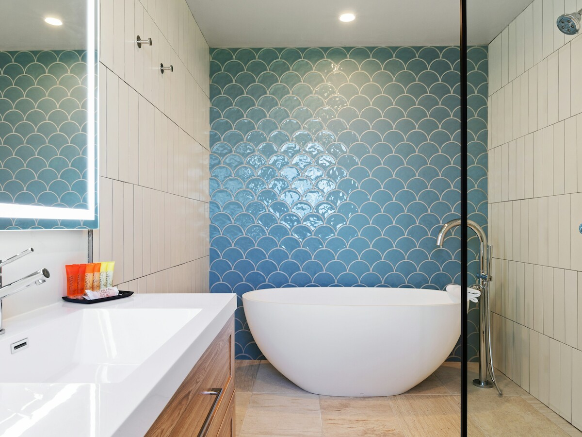 The image shows a modern bathroom with a freestanding tub, blue scallop tiles, and a white vanity with a lit mirror.