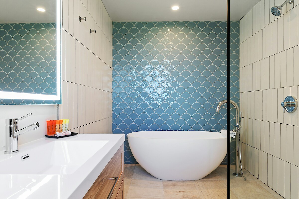 The image shows a modern bathroom with a freestanding tub, blue fish scale tiles, a glass shower, and a vanity with a lit mirror.