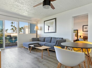 A modern living room with a gray sofa, round table, chairs, and a view of palm trees from the balcony.