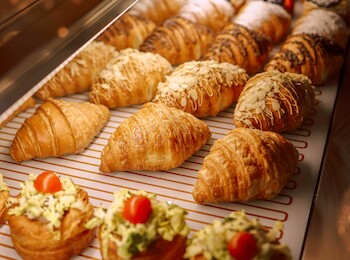 The image shows a display of pastries including croissants and savory tarts with toppings like vegetables and cherry tomatoes in a bakery.