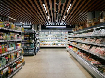 The image shows the interior of a supermarket aisle with shelves stocked with various groceries and products.