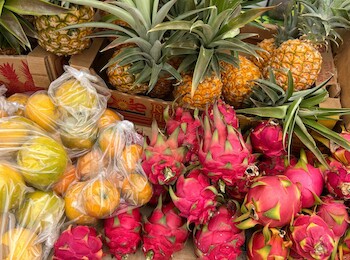 A variety of fruits including pineapples, lemons in bags, and dragon fruits are displayed on a table.